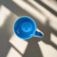 Blue ceramic cup on a metallic surface with a beige background