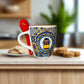 Decorative mug with a tram design and a red spoon on a white surface