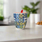 Ceramic mug with colorful pattern and red spoon on a white surface
