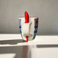 Ceramic mug with colorful patterns and a red handle on a plain surface.