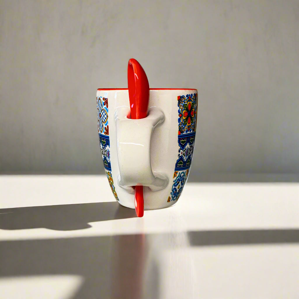 Ceramic mug with colorful patterns and a red handle on a plain surface.