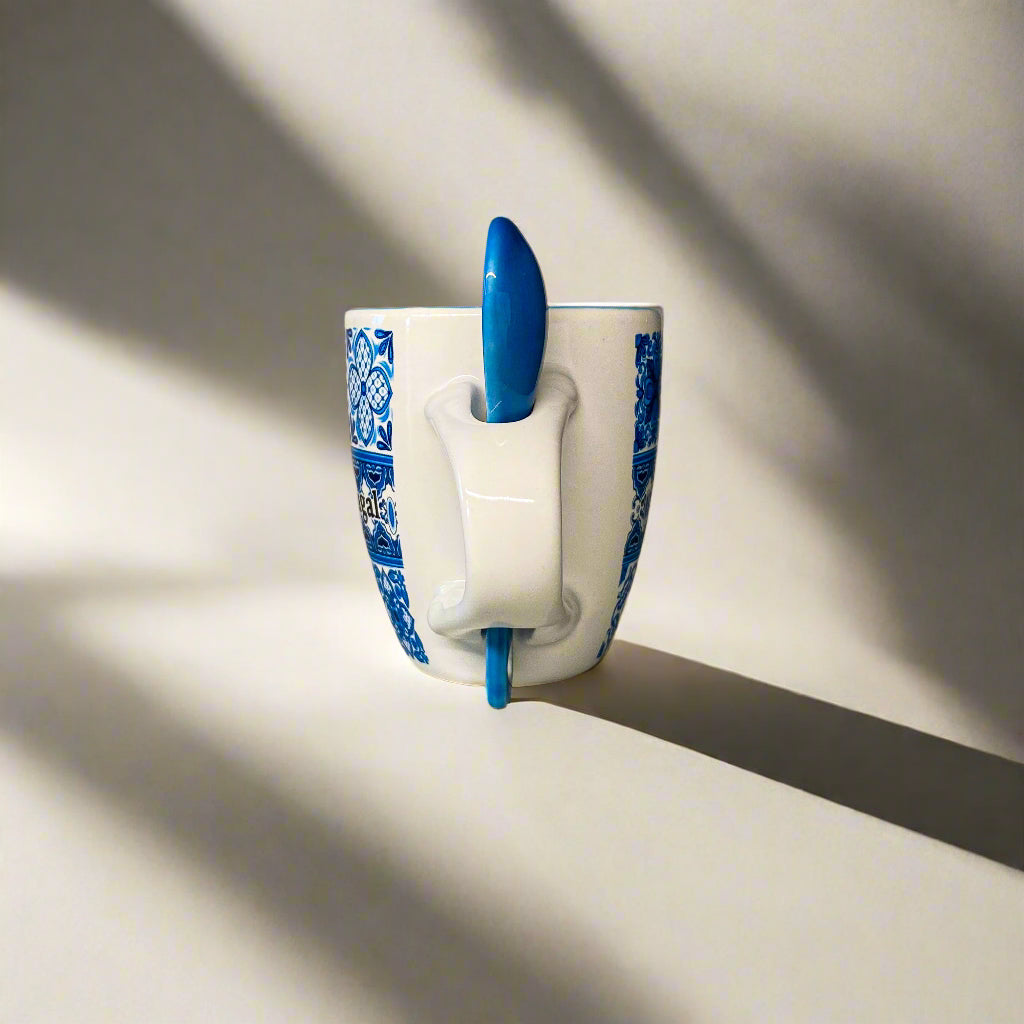 White mug with blue patterns and a blue spoon inside on a light surface.
