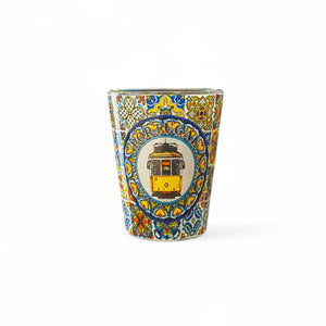 A shot glass with a colorful traditional azulejo tile design featuring a yellow portuguese tram.