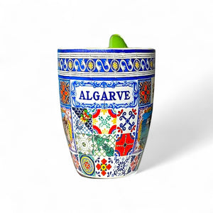 Ceramic Algarve souvenir mug decorated with colorful traditional Portuguese tile patterns and the word "Algarve" in blue, photographed on a white background.