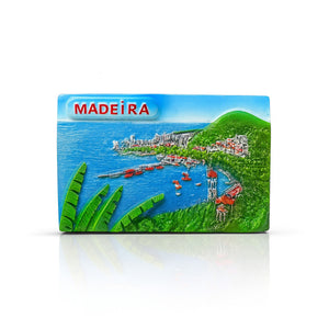 A colorful fridge magnet featuring a panoramic view of a coastal landscape with traditional red fishing boats, green hills, tropical vegetation, and the ocean, with the word 'MADEIRA' prominently displayed.