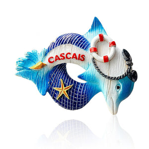 A colorful Cascais souvenir magnet in the shape of a dolphin with nautical motifs including a lifebuoy, anchor, rope, starfish, and seashell.