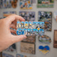 Hand holding a 'Monte Gordo' magnet with scenic design against a background of other magnets.