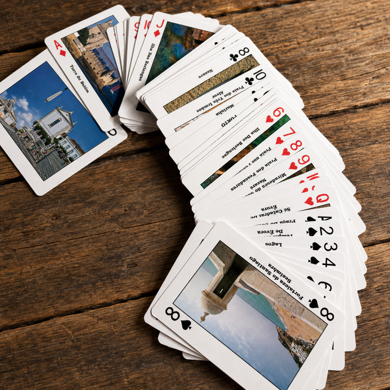 Portugal-themed playing cards on a rustic wooden surface, highlighting Portuguese monuments, beaches, regions, and iconic travel destinations.