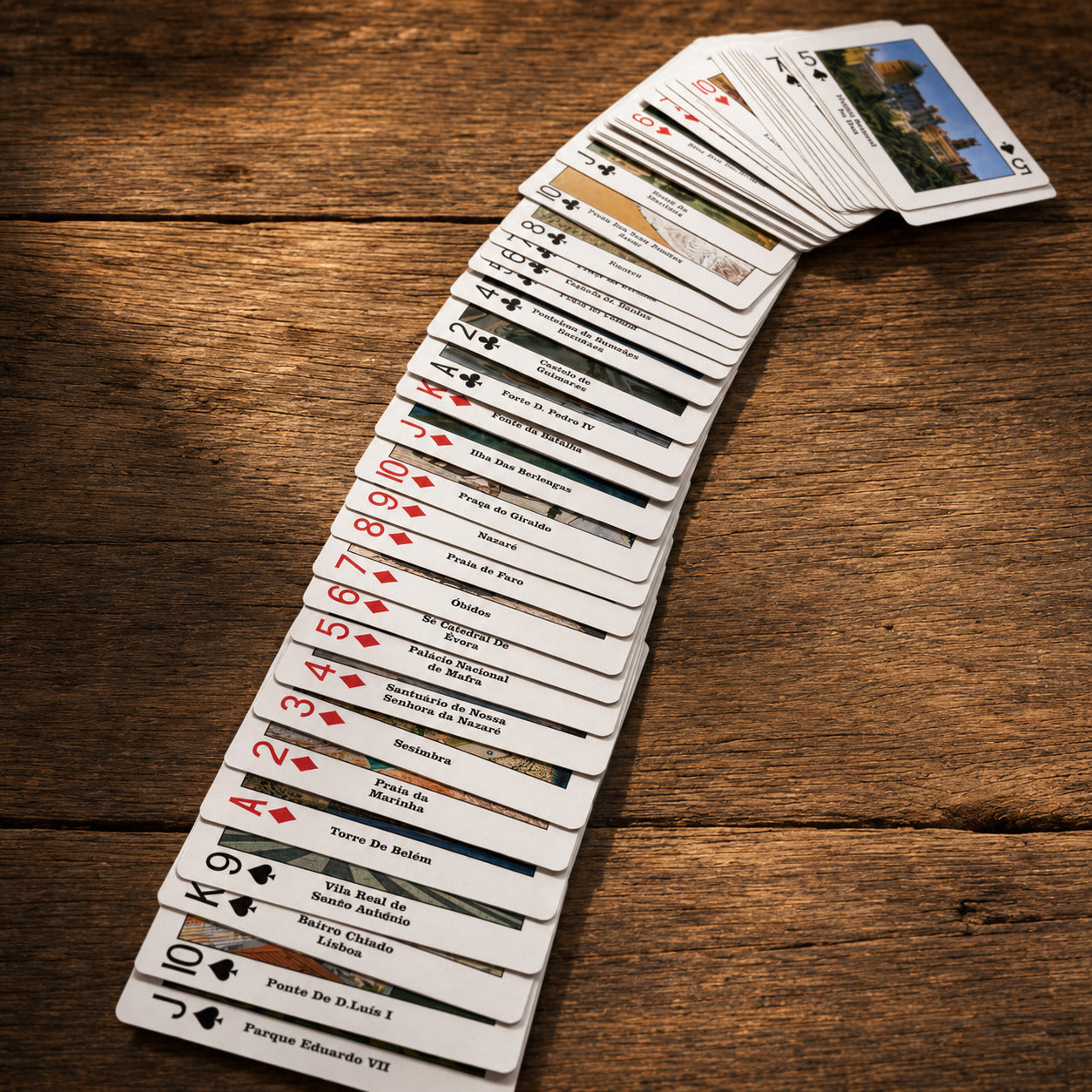 Portugal souvenir playing cards spread across a rustic wooden table, featuring images of Portuguese cities, monuments, beaches, and cultural landmarks.