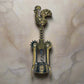 A detailed bronze corkscrew is depicted, featuring a handle shaped like the Barcelos Rooster, a well-known symbol of Portugal. The handle includes a heart design, and the midsection is inscribed with the word "Portugal." This elegant souvenir has two levers and a twisting mechanism.