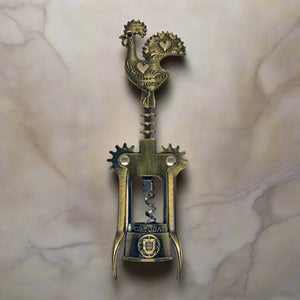 A detailed bronze corkscrew is depicted, featuring a handle shaped like the Barcelos Rooster, a well-known symbol of Portugal. The handle includes a heart design, and the midsection is inscribed with the word "Portugal." This elegant souvenir has two levers and a twisting mechanism.