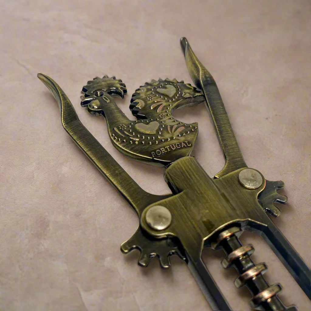 A bronze corkscrew with intricate craftsmanship is presented, with a handle modeled after the Barcelos Rooster, a symbol strongly linked to Portugal. The rooster's design incorporates a heart, and the word "Portugal" is etched into the midsection. The corkscrew includes two levers and a rotating mechanism.