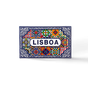 A rectangular ceramic tile with brightly colored geometric and floral patterns, predominantly in blue, red, yellow, and green. The center features the word "LISBOA" in bold blue letters on a white background, surrounded by intricate decorative designs. Perfect as a Lisbon souvenir magnet.