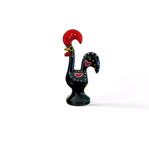 A black and red rooster figurine, a souvenir from Portugal, displayed on a table, symbolizing the Galo de Barcelos.