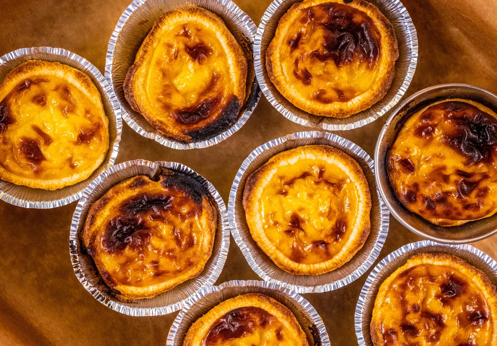 Group of freshly baked Lisbon pastel de nata with caramelized tops in aluminum molds